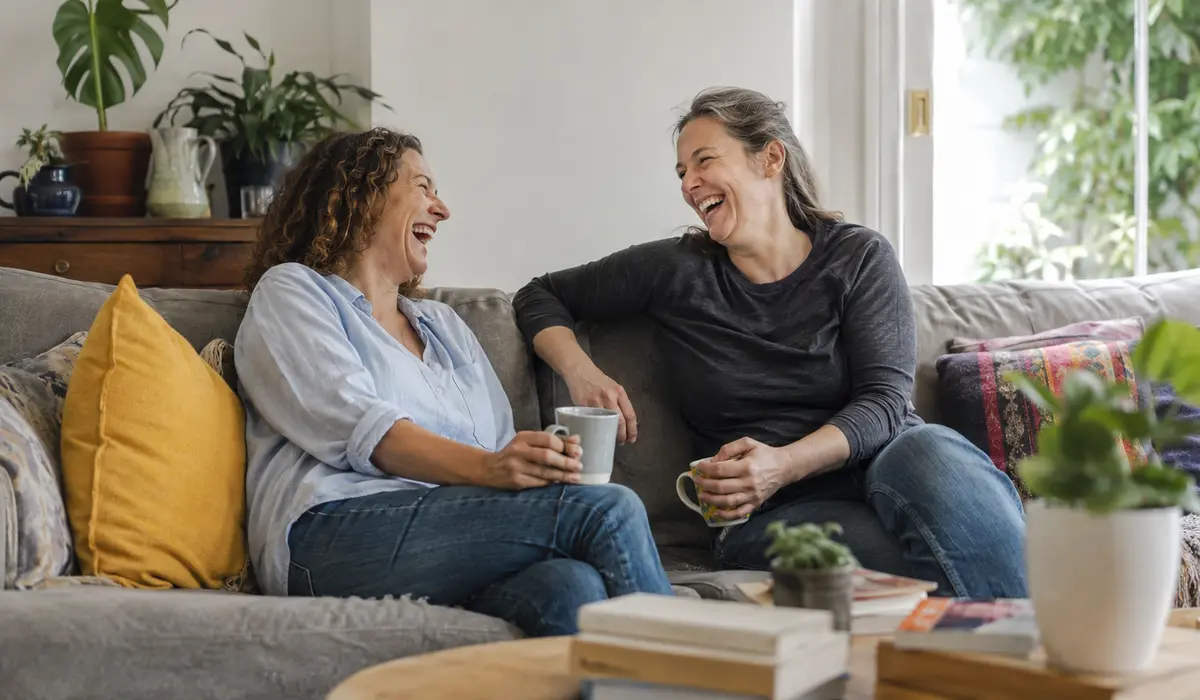 Two friends laughing together in a bright living room.